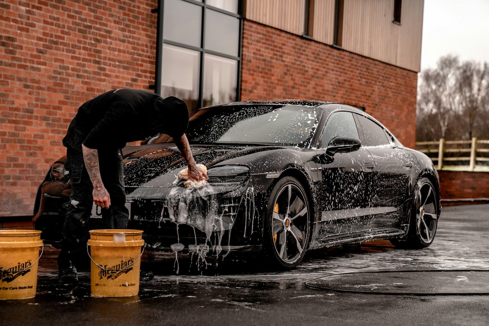 Detailer hand-washing a black sports car with foam before coating